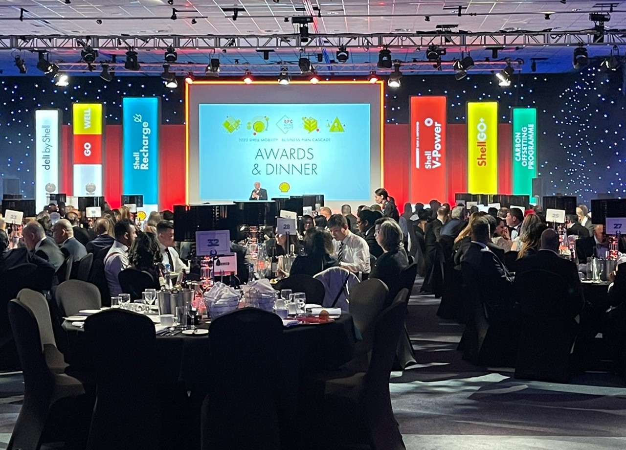 Guests at an awards dinner with a brightly lit presentation stage